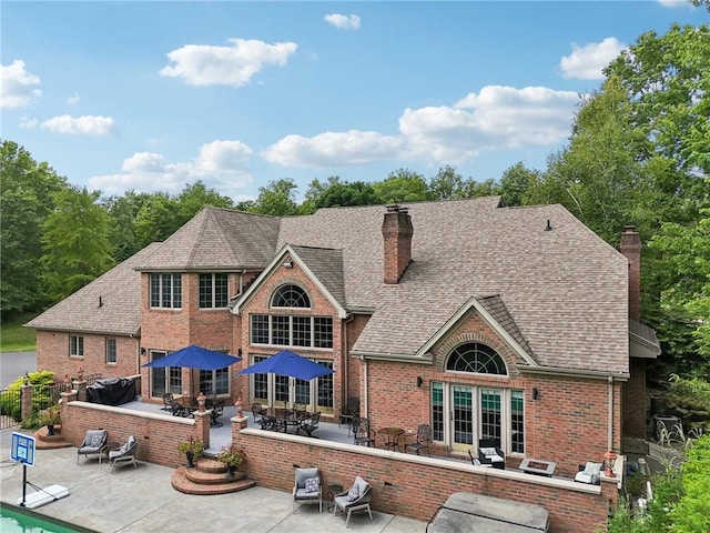 back of property with brick siding, a chimney, a shingled roof, outdoor dining space, and a patio area