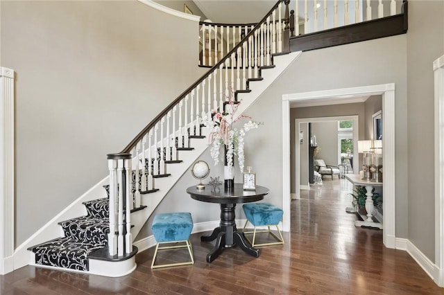 foyer entrance with stairway, a high ceiling, baseboards, and wood finished floors