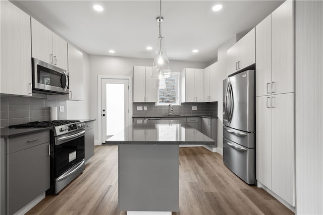 kitchen with stainless steel appliances, a kitchen island, pendant lighting, light hardwood / wood-style floors, and white cabinets