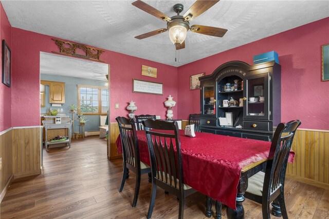 dining room featuring wood walls, a textured ceiling, wood-type flooring, ceiling fan, and a baseboard radiator