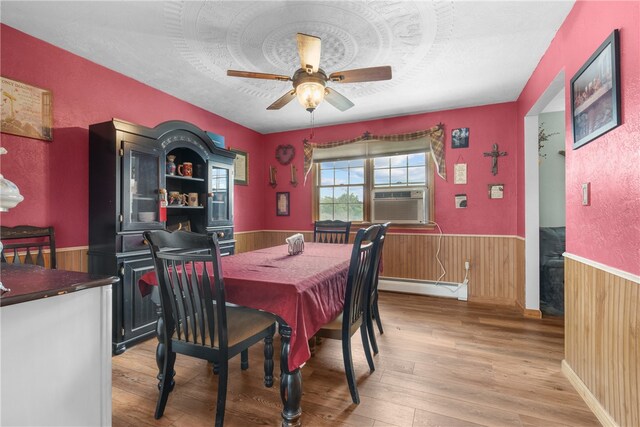 dining room with wooden walls, a baseboard heating unit, ceiling fan, and hardwood / wood-style flooring