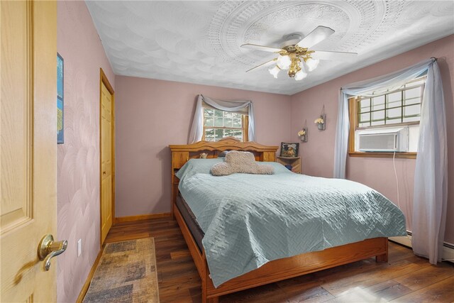 bedroom with cooling unit, a baseboard heating unit, dark hardwood / wood-style floors, and ceiling fan