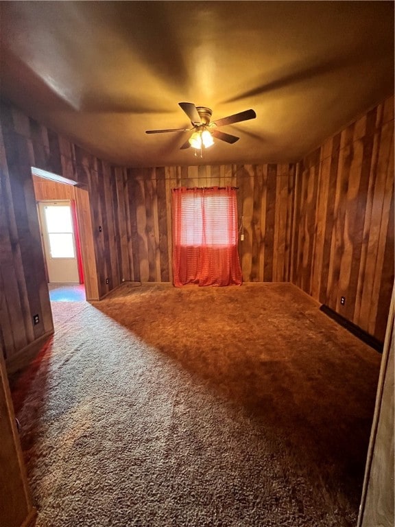 unfurnished room featuring ceiling fan, carpet, and wood walls