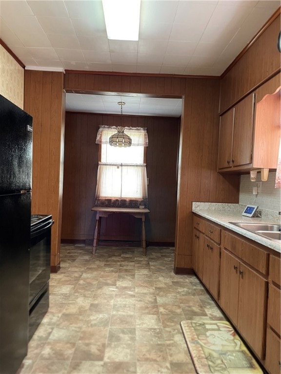 kitchen featuring sink, wooden walls, pendant lighting, light tile patterned floors, and black fridge