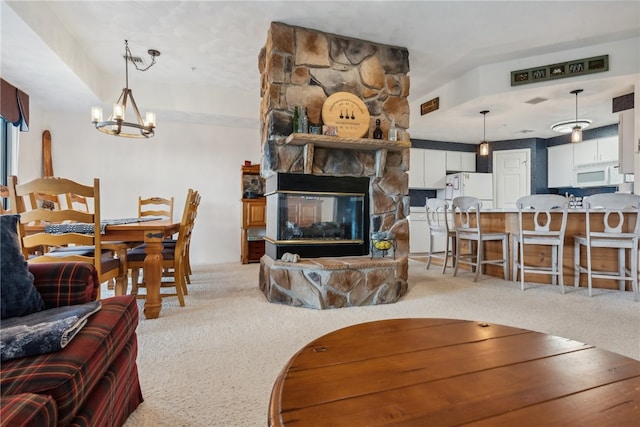 living room with carpet, a stone fireplace, and an inviting chandelier