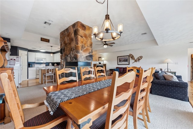 carpeted dining room featuring a raised ceiling and ceiling fan with notable chandelier