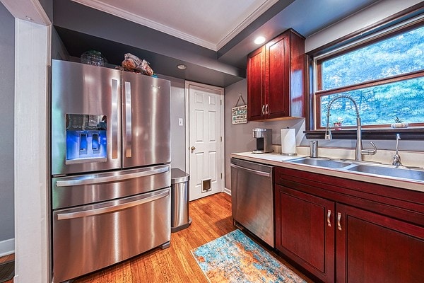 kitchen with sink, light wood-type flooring, crown molding, and stainless steel appliances