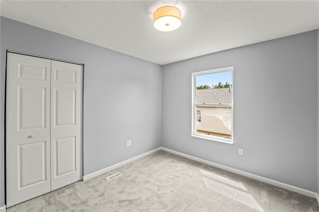 unfurnished bedroom with baseboards, visible vents, a closet, and light colored carpet