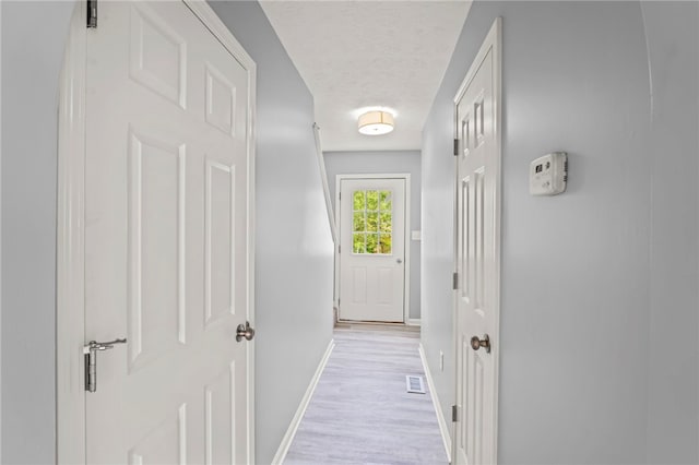 hallway with light hardwood / wood-style flooring and a textured ceiling