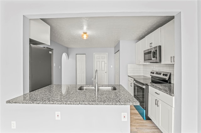 kitchen with a peninsula, a sink, white cabinets, appliances with stainless steel finishes, and light stone countertops