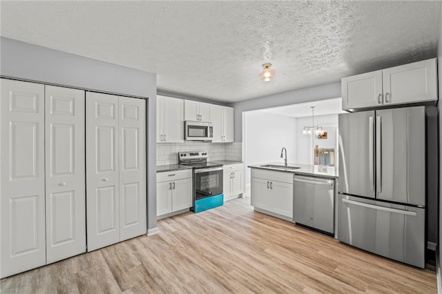 kitchen featuring a sink, white cabinets, hanging light fixtures, appliances with stainless steel finishes, and light wood finished floors