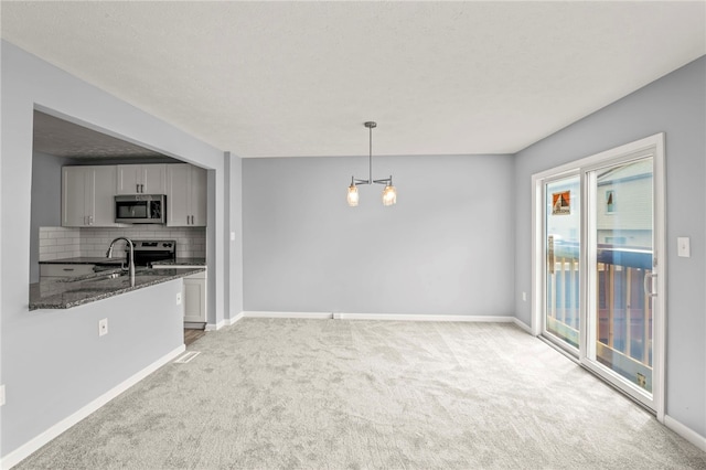 kitchen featuring gray cabinetry, light colored carpet, stainless steel appliances, hanging light fixtures, and dark stone countertops