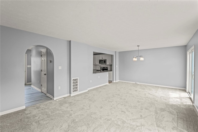 unfurnished living room featuring light colored carpet, visible vents, arched walkways, and a chandelier