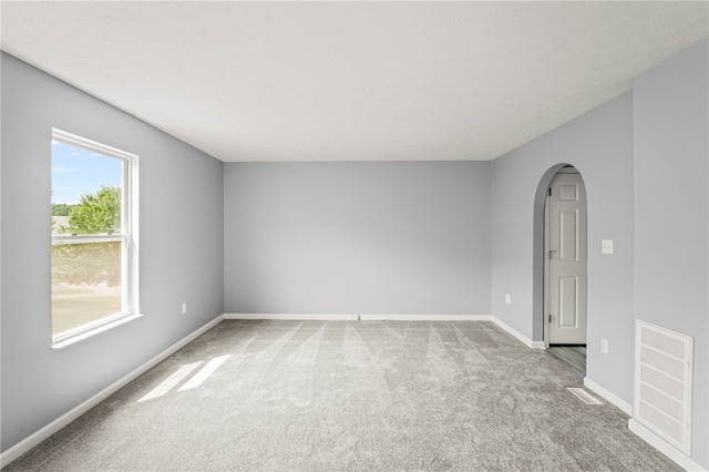 spare room featuring baseboards, visible vents, arched walkways, and light colored carpet