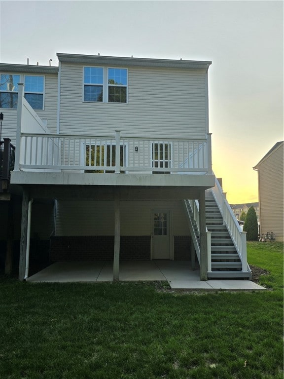 back house at dusk featuring a patio area, a deck, and a yard