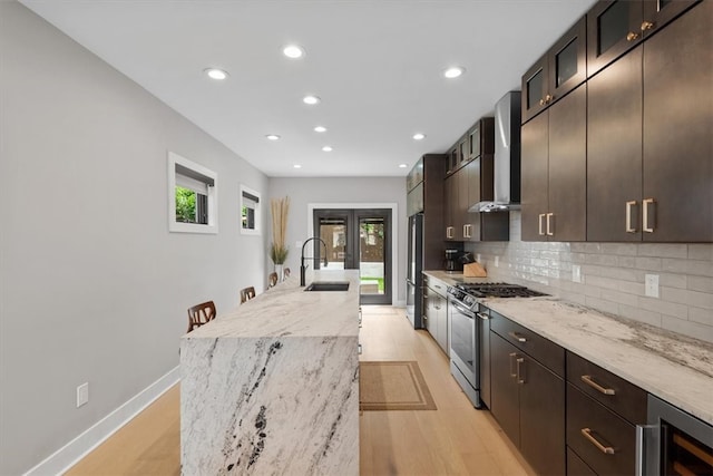 kitchen featuring sink, wall chimney range hood, light hardwood / wood-style floors, stainless steel appliances, and light stone counters