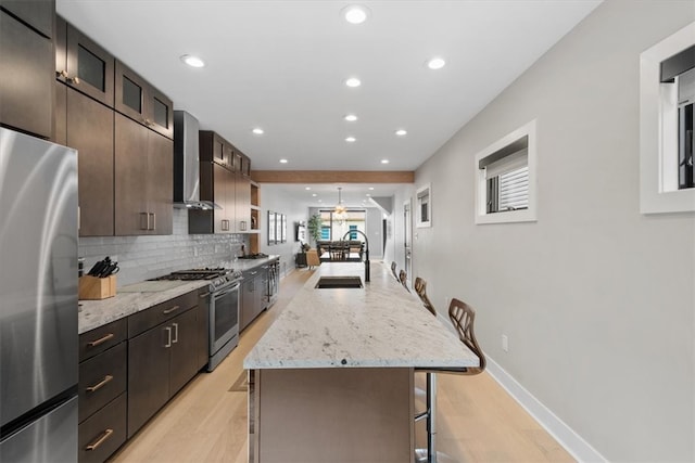 kitchen featuring sink, wall chimney range hood, a kitchen breakfast bar, a kitchen island, and appliances with stainless steel finishes