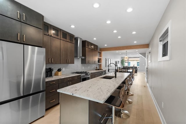 kitchen featuring a kitchen bar, appliances with stainless steel finishes, wall chimney exhaust hood, sink, and a center island with sink