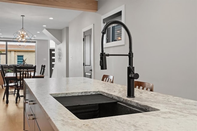 kitchen with sink, hanging light fixtures, beamed ceiling, a notable chandelier, and light wood-type flooring