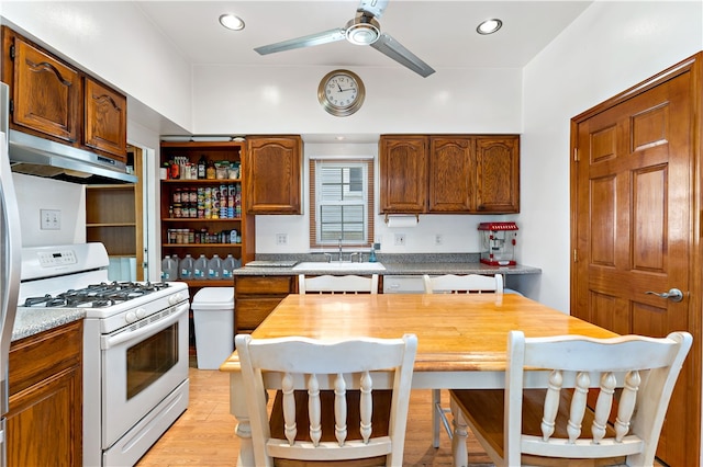 kitchen featuring light wood-type flooring, white gas range, ceiling fan, sink, and a kitchen bar