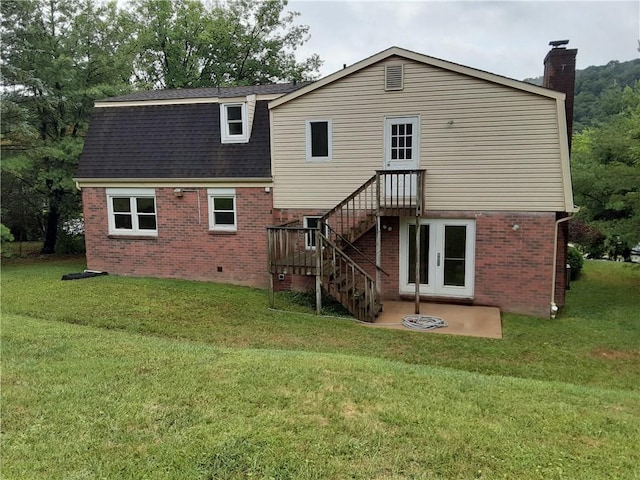 back of property with brick siding, roof with shingles, a chimney, a lawn, and stairway