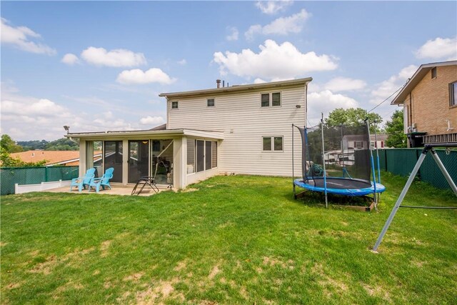 back of house featuring a lawn, a sunroom, a patio, and a trampoline