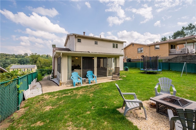 rear view of house featuring a fire pit, a trampoline, a patio, and a yard