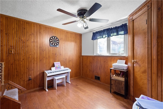 misc room featuring ceiling fan, a textured ceiling, wooden walls, and light hardwood / wood-style flooring