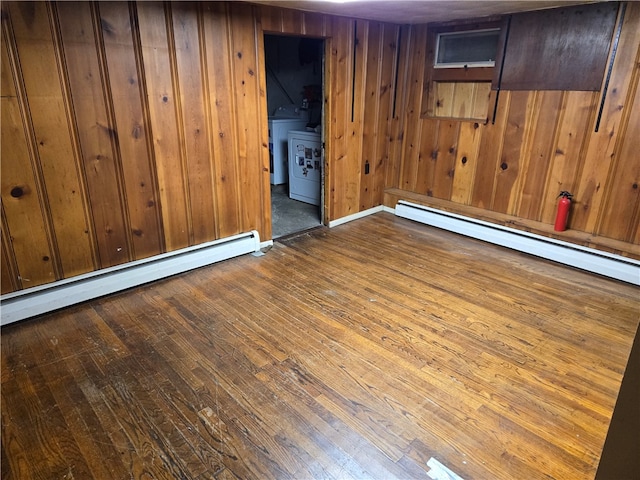 empty room featuring baseboard heating, wood walls, washing machine and dryer, and hardwood / wood-style flooring