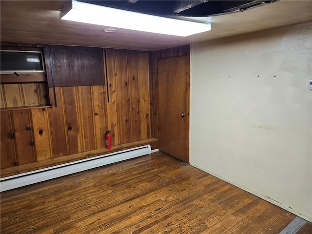 spare room featuring wooden walls, dark hardwood / wood-style flooring, and a baseboard heating unit