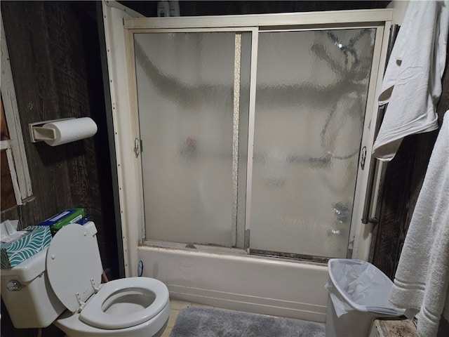 bathroom with toilet and bath / shower combo with glass door