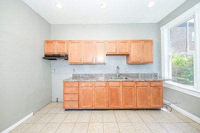 kitchen with tasteful backsplash, range hood, light stone countertops, light tile patterned floors, and sink