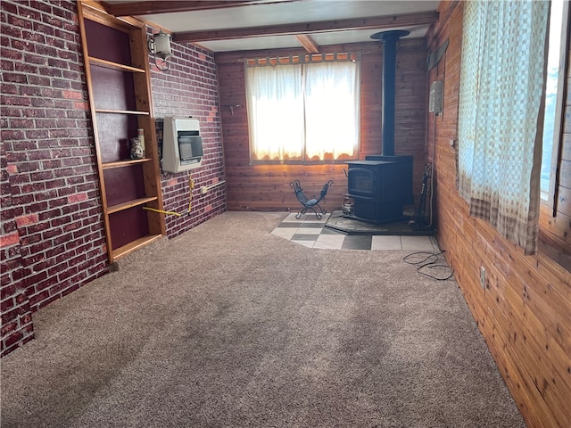 interior space with light colored carpet, wood walls, a wood stove, beamed ceiling, and brick wall