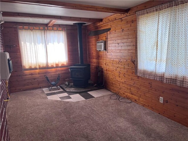 unfurnished living room with beamed ceiling, wooden walls, light carpet, and a wood stove