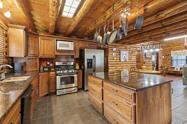 kitchen featuring sink, rustic walls, appliances with stainless steel finishes, beamed ceiling, and a kitchen island