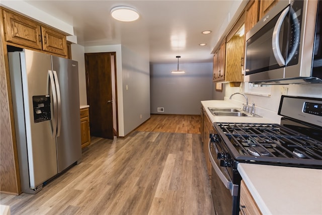 kitchen with light wood-type flooring, sink, stainless steel appliances, and hanging light fixtures