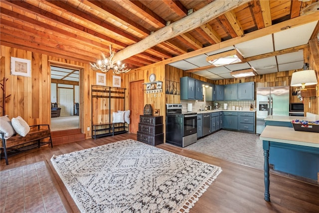 kitchen with appliances with stainless steel finishes, beamed ceiling, wood-type flooring, and an inviting chandelier