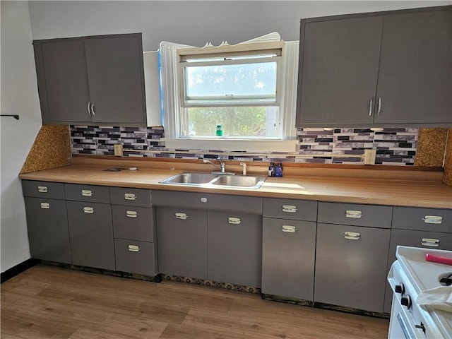 kitchen featuring tasteful backsplash, light countertops, gray cabinetry, a sink, and light wood-type flooring