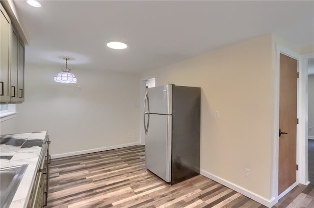 kitchen featuring light wood-type flooring, stainless steel refrigerator, gray cabinetry, sink, and decorative light fixtures