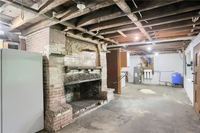 basement featuring water heater, white refrigerator, and brick wall