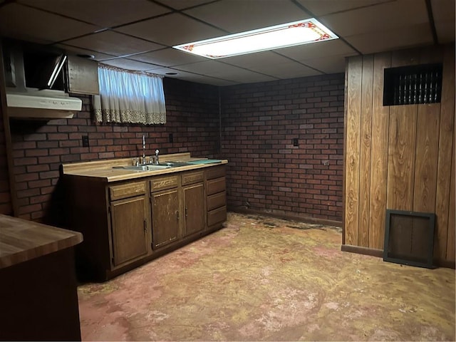 kitchen with sink, a drop ceiling, wood counters, brick wall, and dark brown cabinets