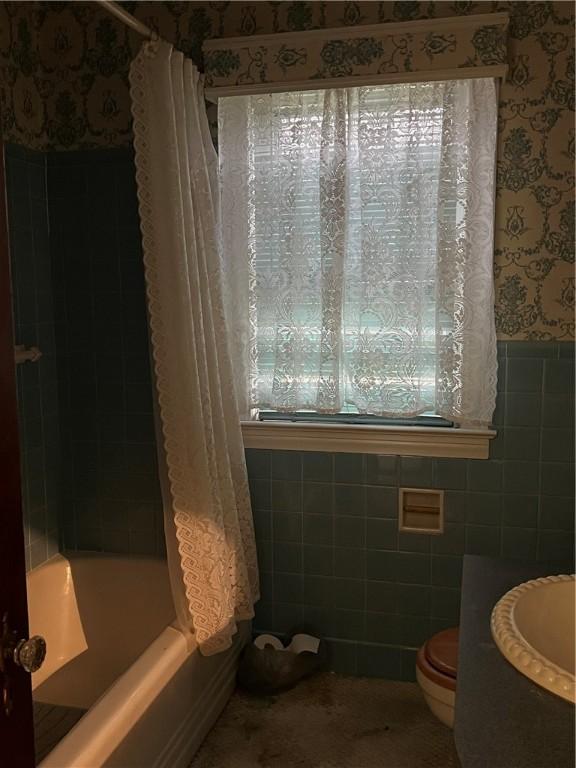 full bathroom featuring sink, shower / bathtub combination with curtain, tile walls, and toilet