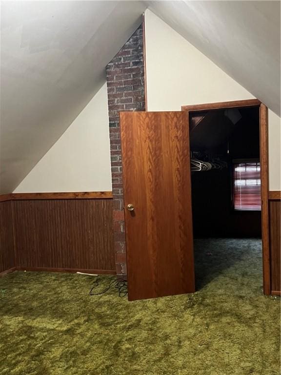 additional living space with wood walls, lofted ceiling, and dark colored carpet