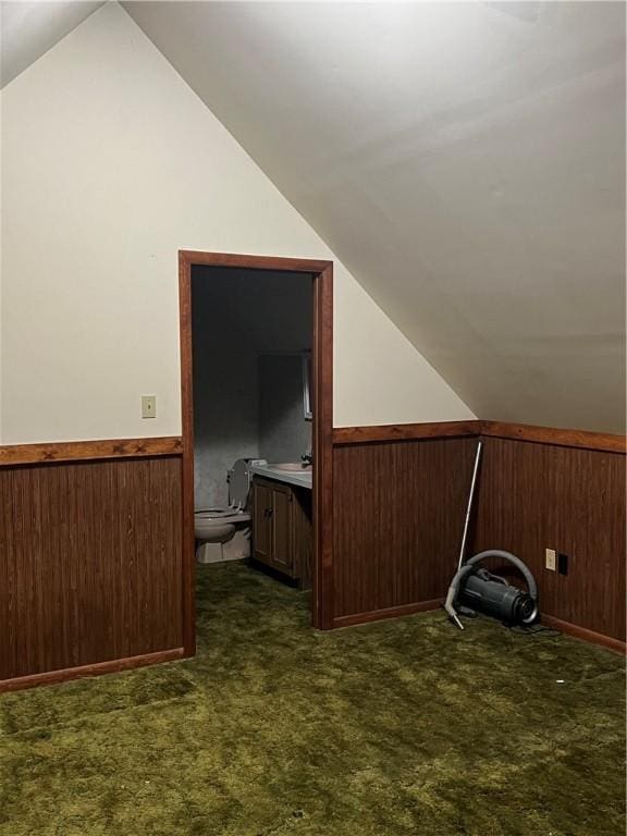 additional living space with wooden walls, vaulted ceiling, and dark colored carpet