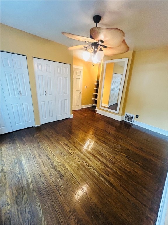 unfurnished bedroom featuring ceiling fan, dark wood-type flooring, and multiple closets