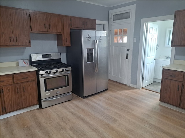 kitchen with appliances with stainless steel finishes, crown molding, and light hardwood / wood-style flooring