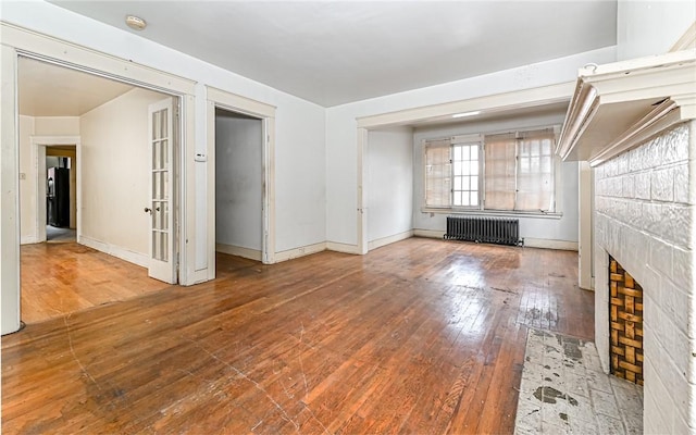 unfurnished living room featuring a tiled fireplace, radiator heating unit, and wood-type flooring