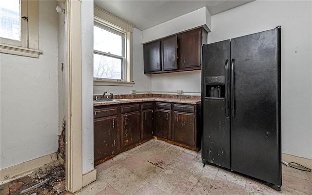 kitchen featuring black fridge with ice dispenser, plenty of natural light, dark brown cabinets, and sink