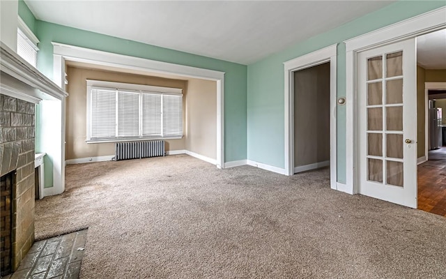 unfurnished living room with carpet flooring, radiator heating unit, french doors, and a fireplace