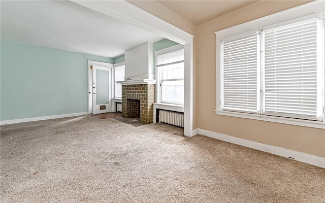 unfurnished living room with carpet flooring, radiator heating unit, and a brick fireplace